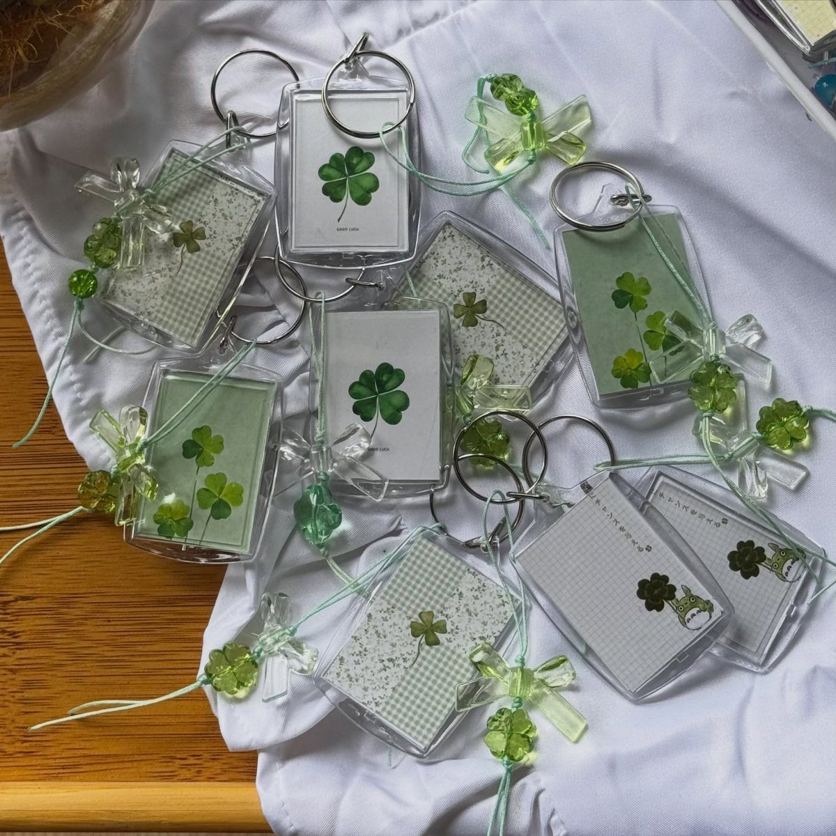 Four leaf clover keychains in clear acrylic cases with green ribbons on white fabric