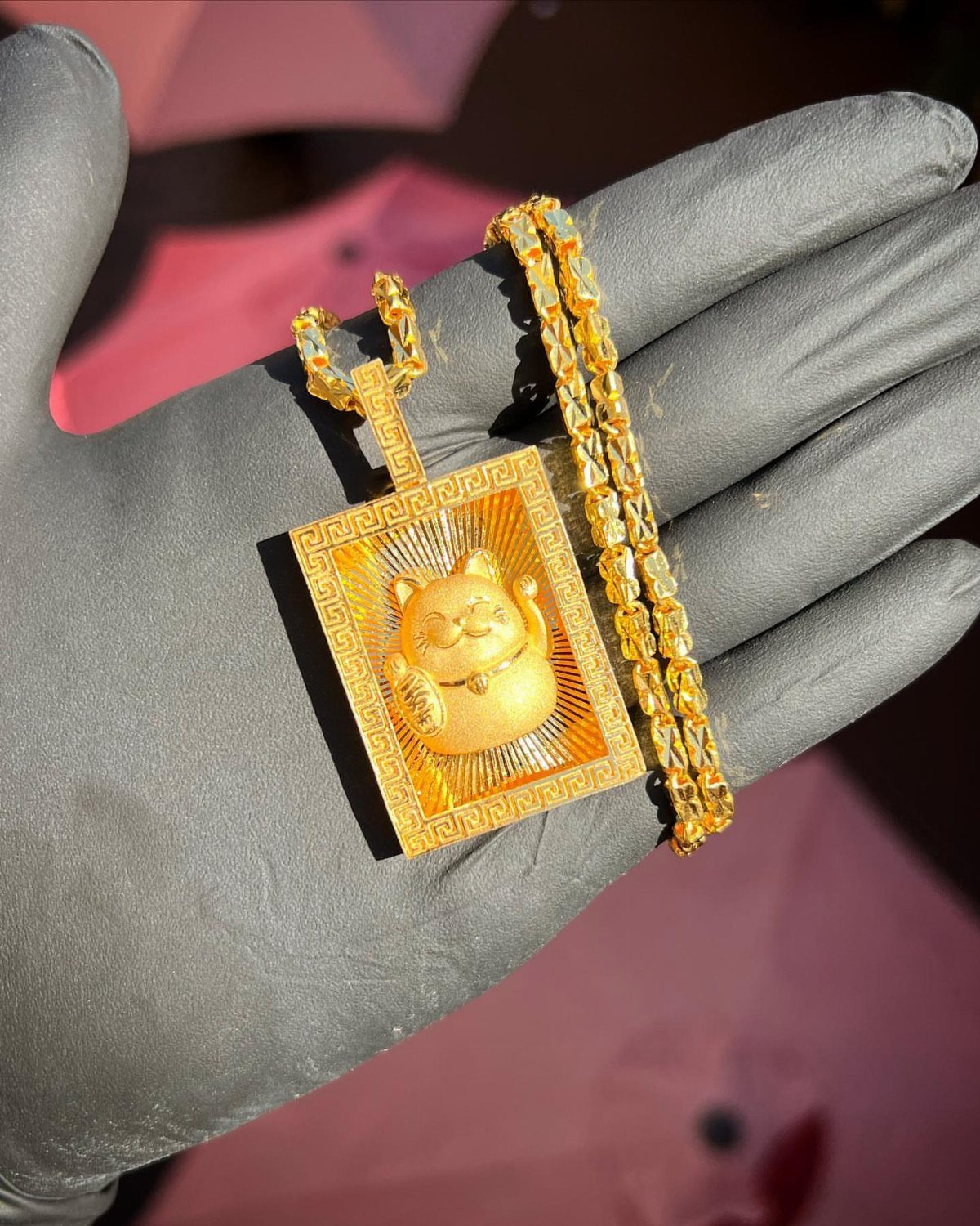 Gold lucky cat pendant and chain held in a black gloved hand.