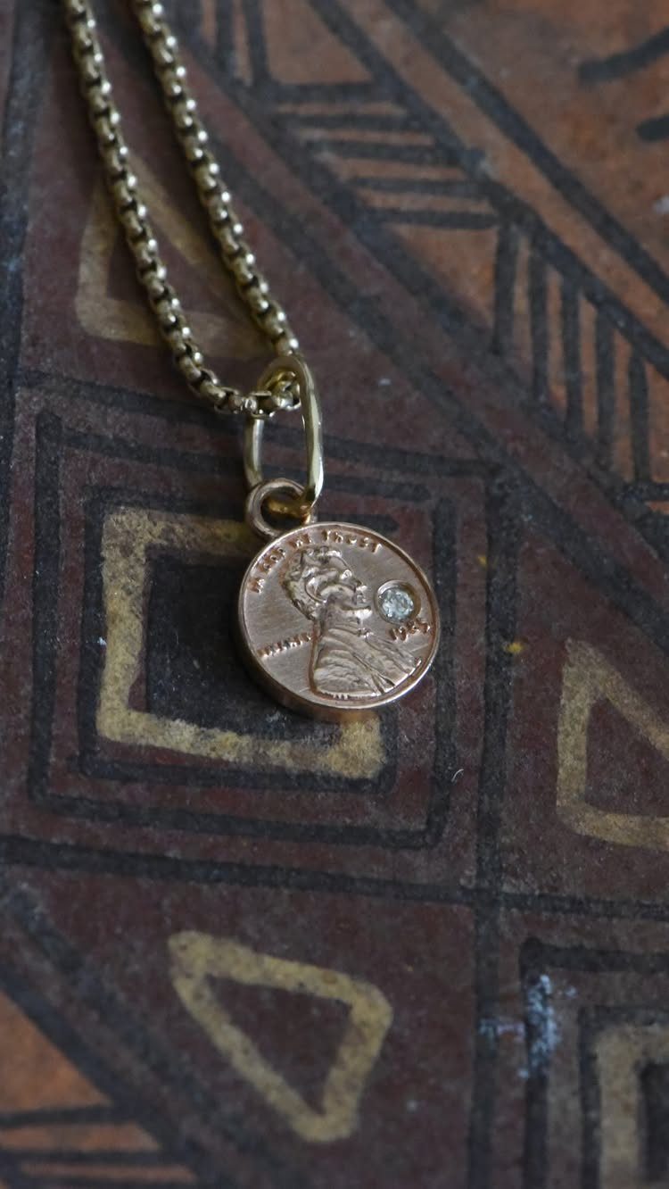 Gold coin pendant necklace with a small diamond on a patterned brown surface