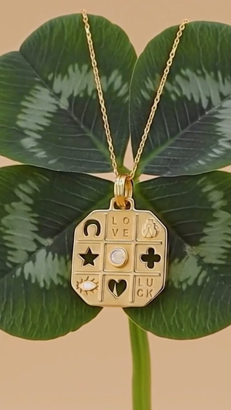 Gold symbol pendant necklace resting on a green four-leaf clover leaf