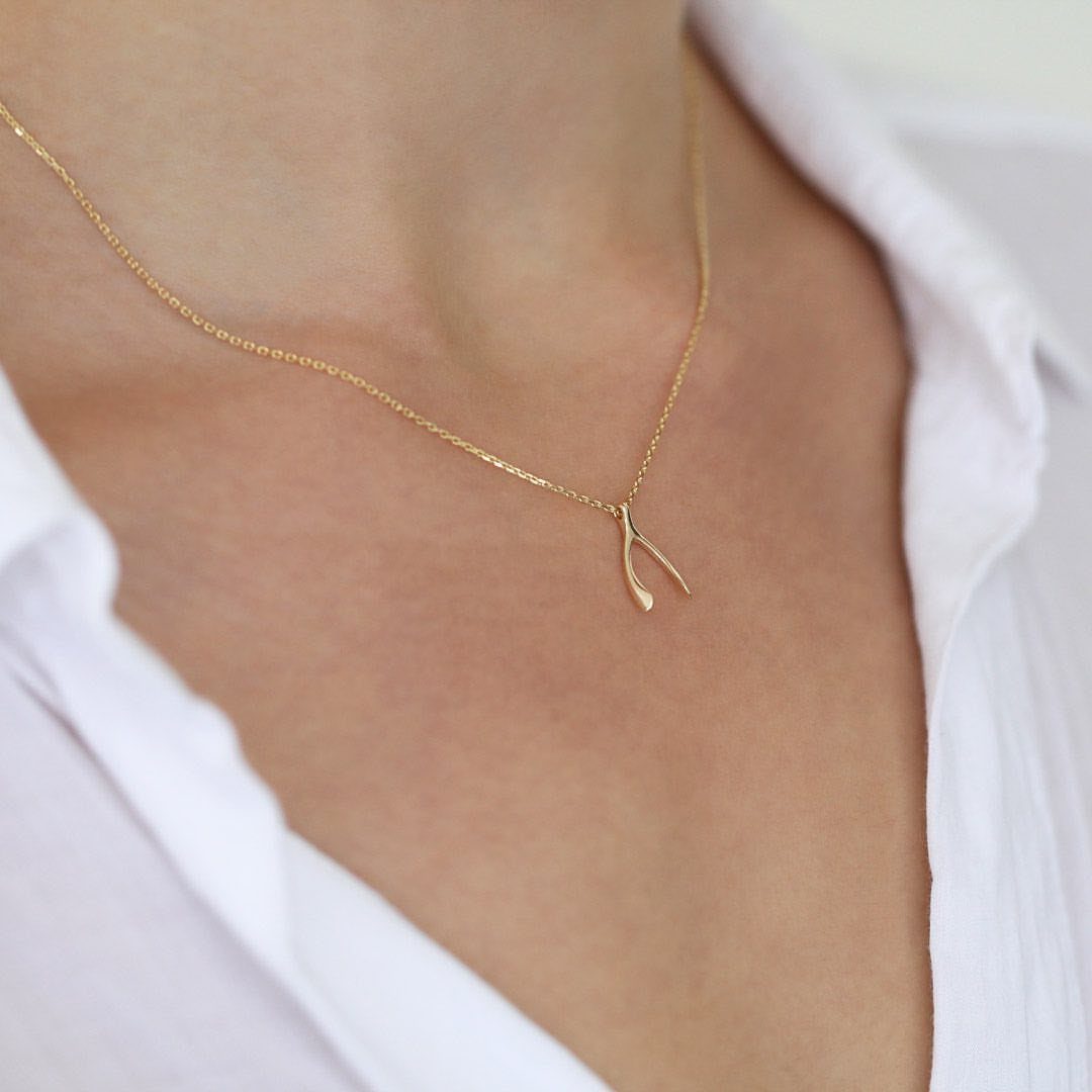 Gold wishbone necklace worn on a person wearing a white collared shirt