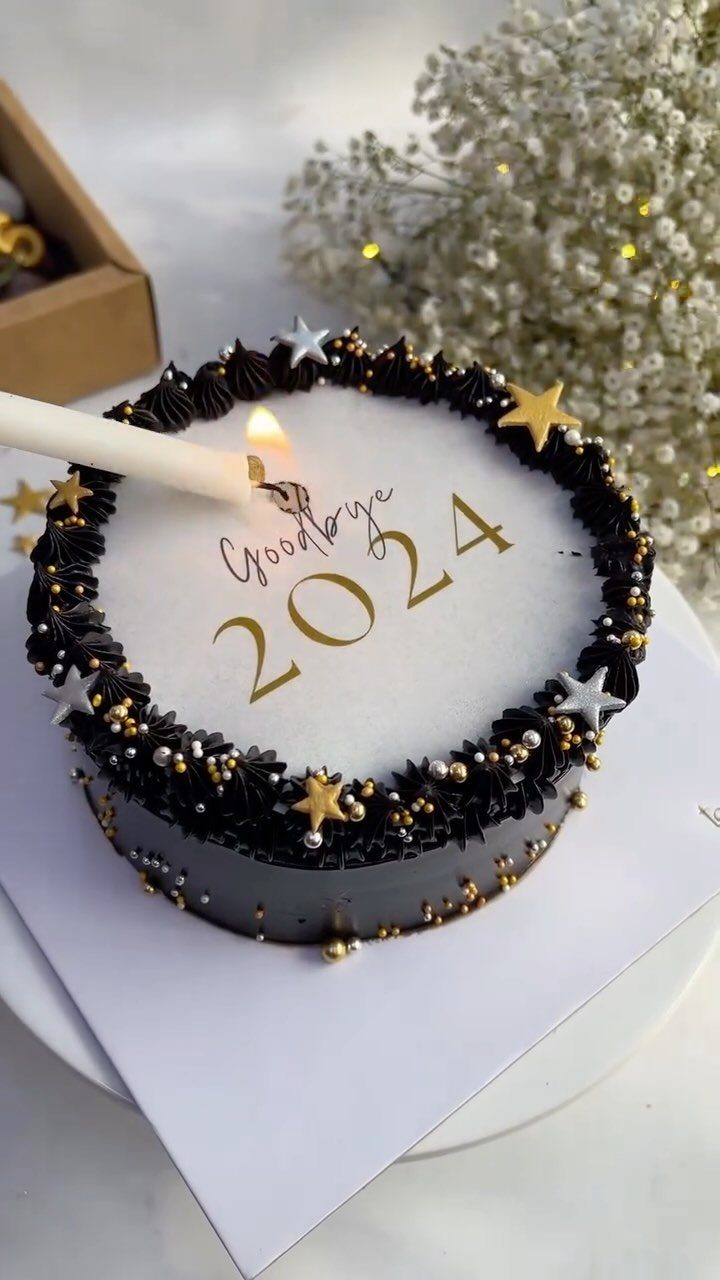 Small white and black New Year cake with gold stars and lit candle