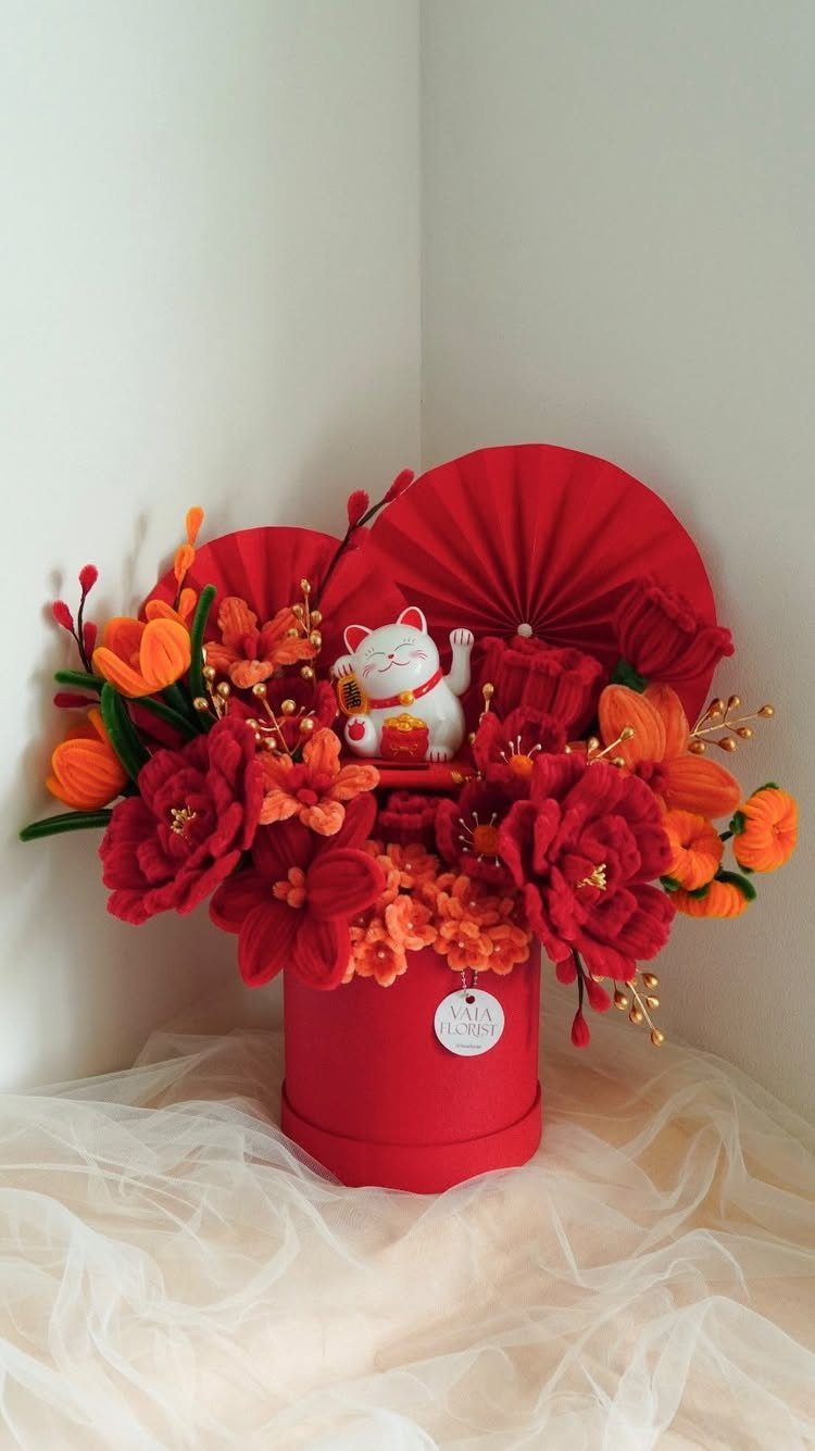 Red gift box with orange and red artificial flowers and a lucky cat figurine.