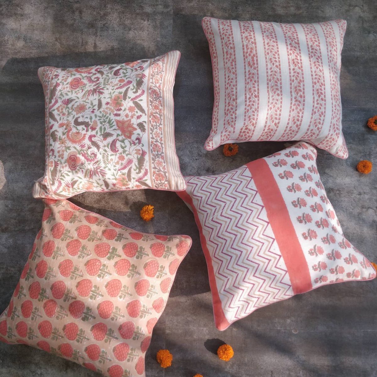 Four printed cushions with red floral and geometric patterns on a grey surface.