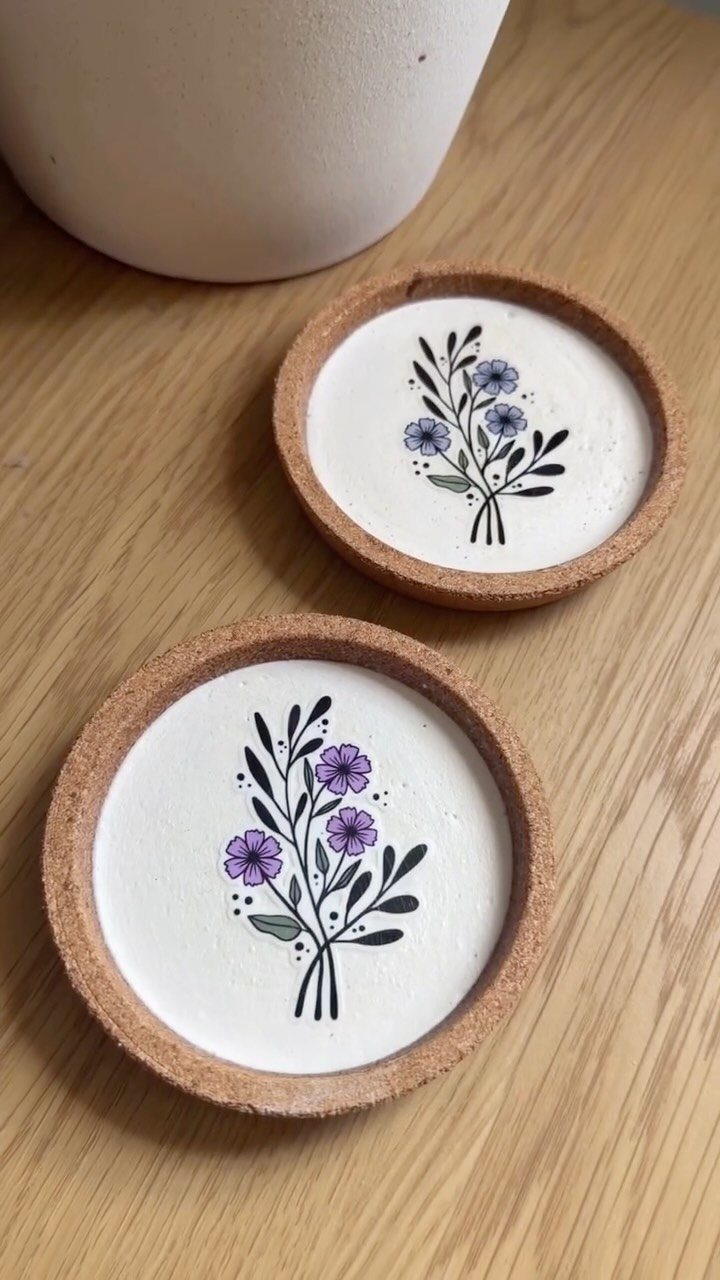 Two floral coasters with cork borders resting on a light wooden table.