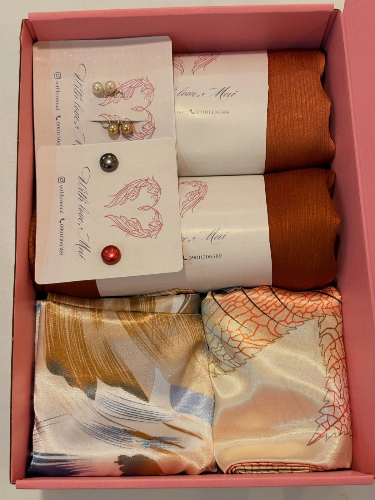 Gift box with orange and patterned silk scarves and pearl stud earrings.