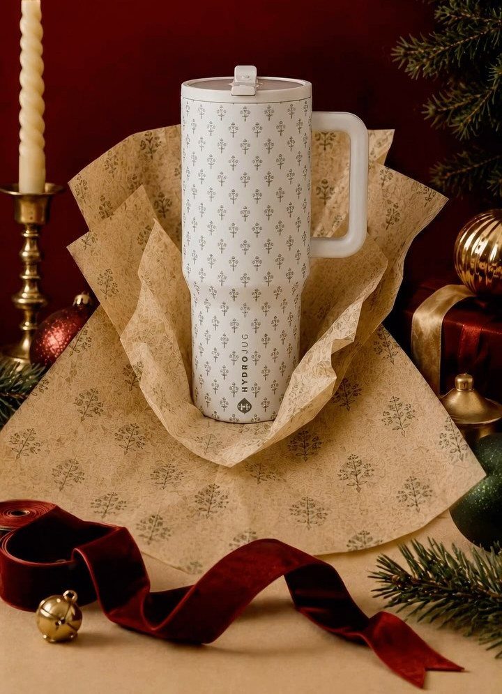 White patterned travel mug wrapped in gold tissue paper with holiday decorations.