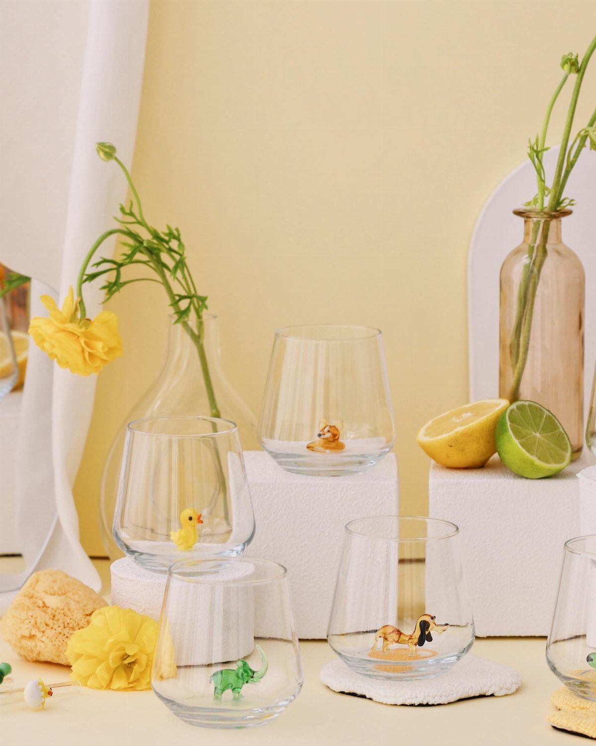 Stemless glasses with animal figurines arranged with yellow flowers and citrus fruits.
