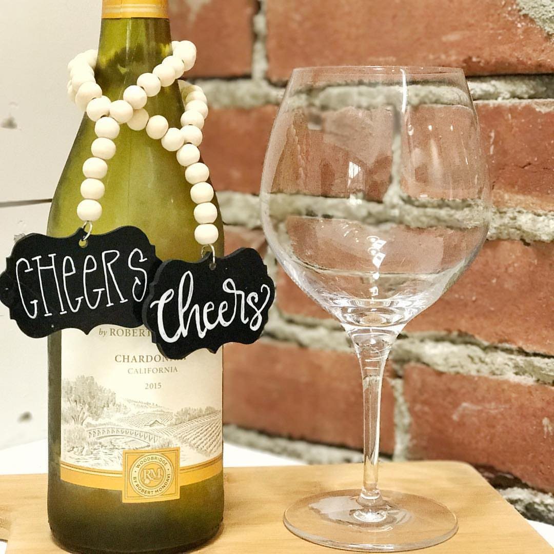 Bottle of white wine with decorative beads and cheers tags next to a glass.