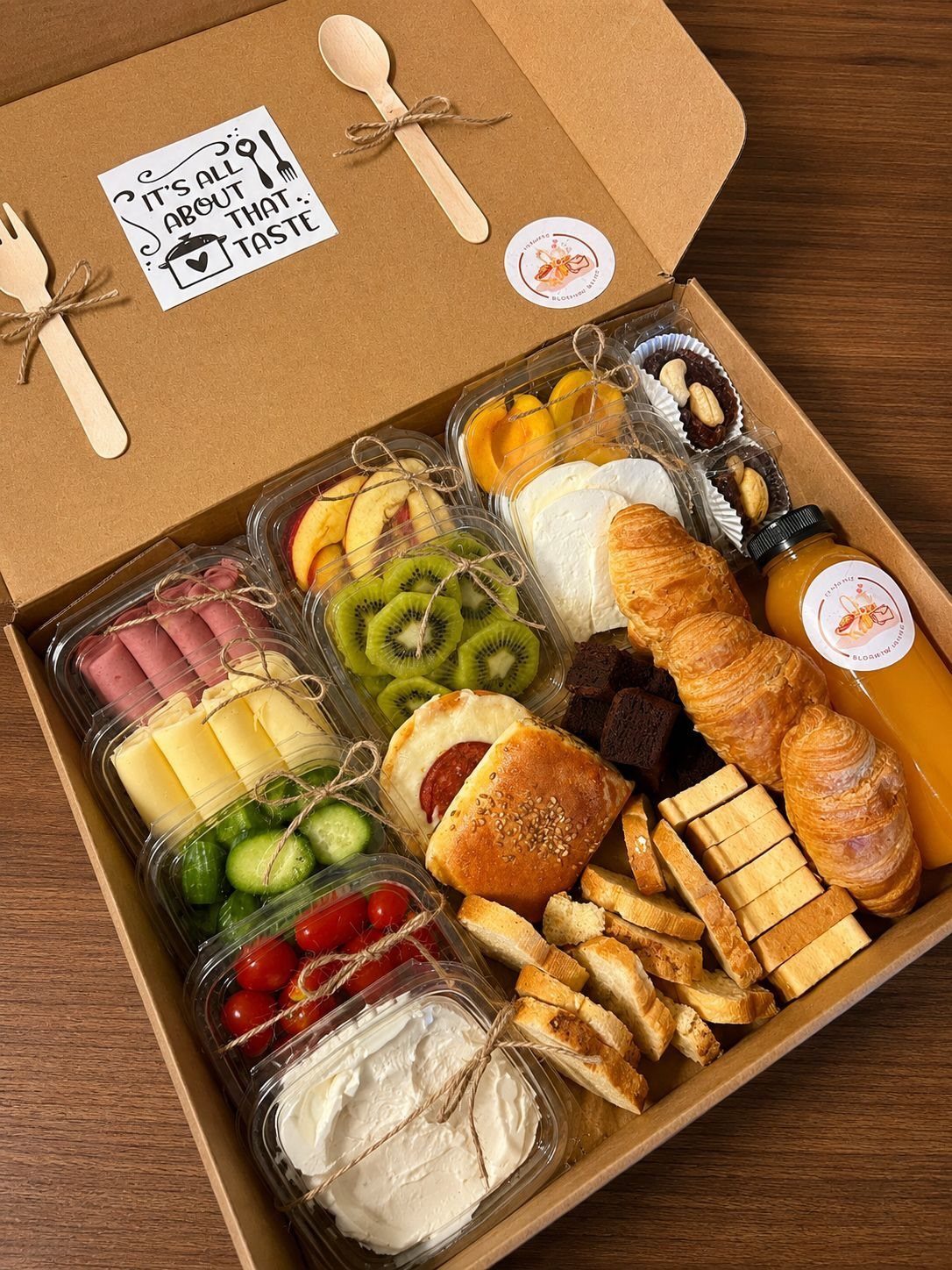 Breakfast box with croissants, fresh fruit, cheese, meats, and orange juice.