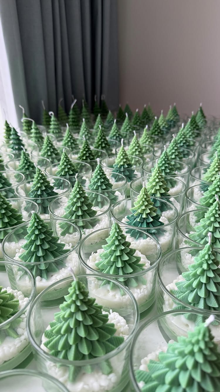 Green Christmas tree shaped candles in small glass jars arranged in rows.