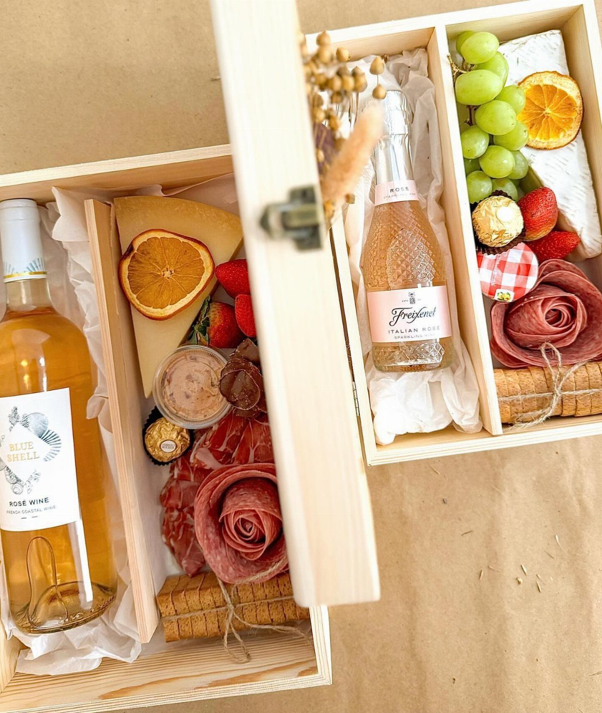 Wooden gift boxes with wine, cured meat roses, cheese, and fresh fruit.
