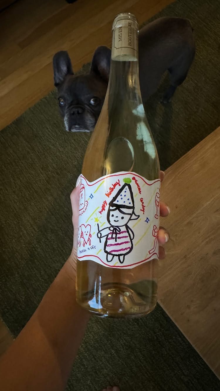 Wine bottle with a hand-drawn custom birthday label held in front of a dog