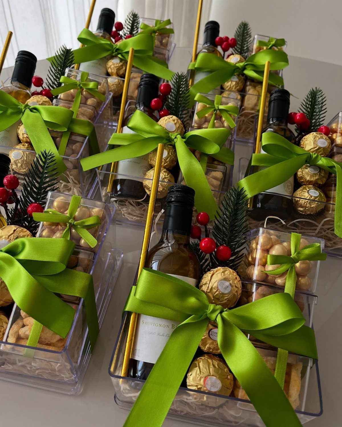 Wine gift baskets in clear plastic containers with green ribbons and gold chocolates.