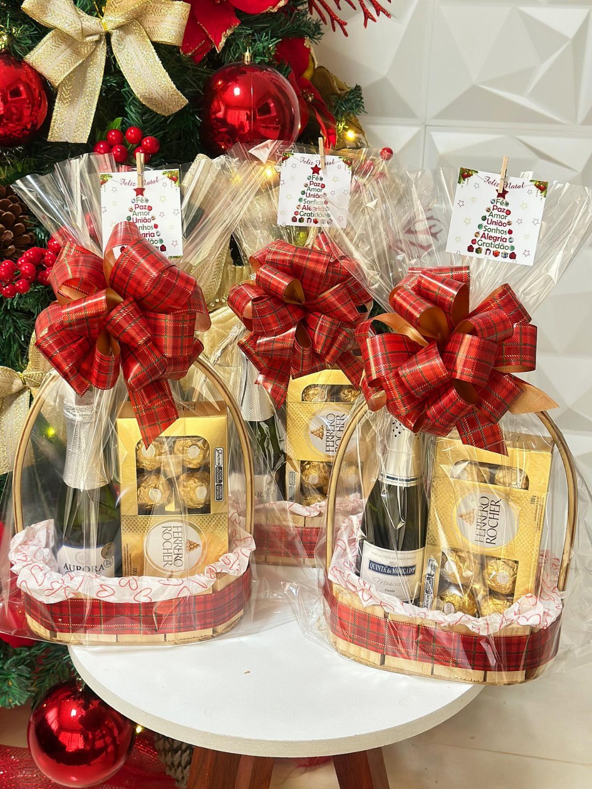 Three wine gift baskets in wicker containers with red bows and chocolates.