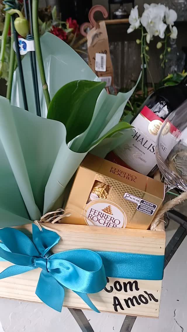 Gift box with wine, Ferrero Rocher chocolates, and green foliage tied with blue ribbon
