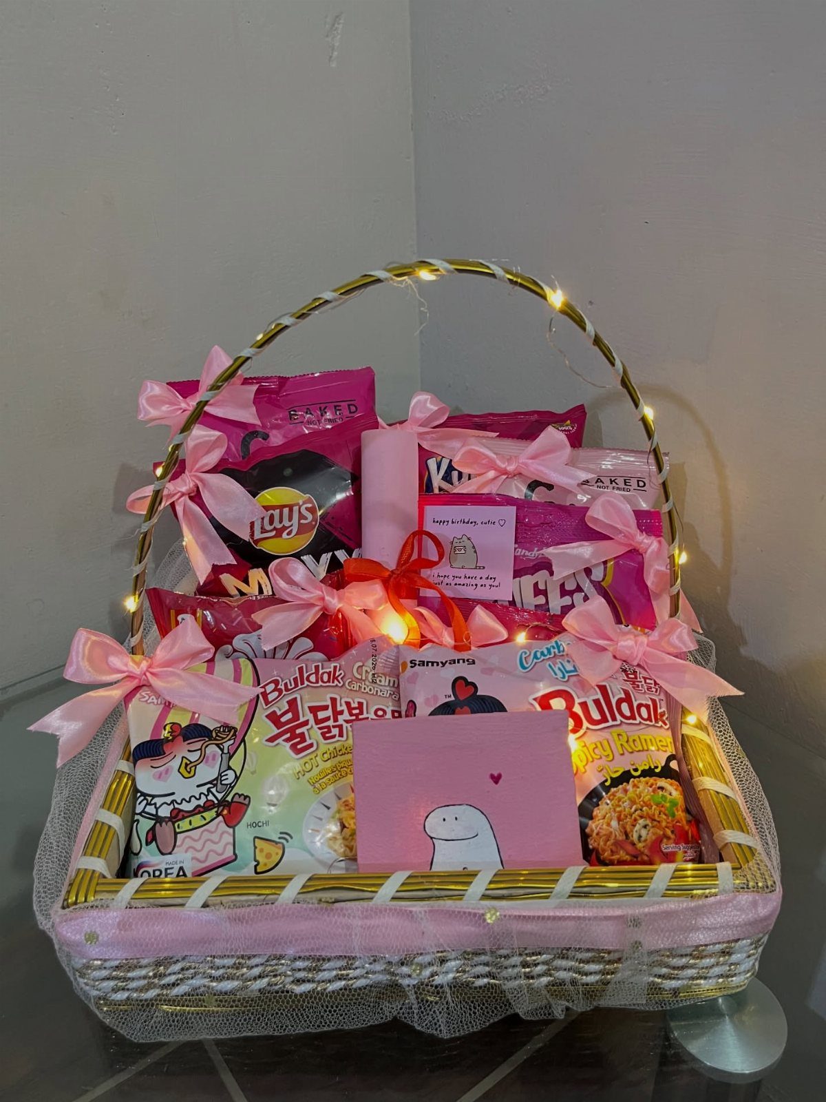 Snack basket filled with pink packaged treats, decorated with ribbons and fairy lights.