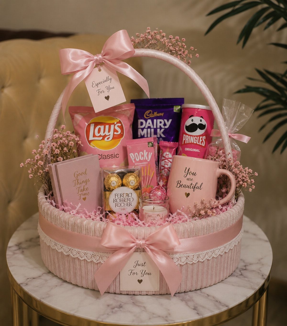 Pink snack gift basket filled with chips, chocolates, and a mug on a table