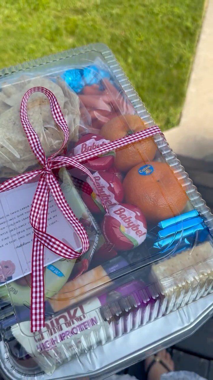 Clear plastic snack container with cheese, oranges, and protein bars tied with ribbon.