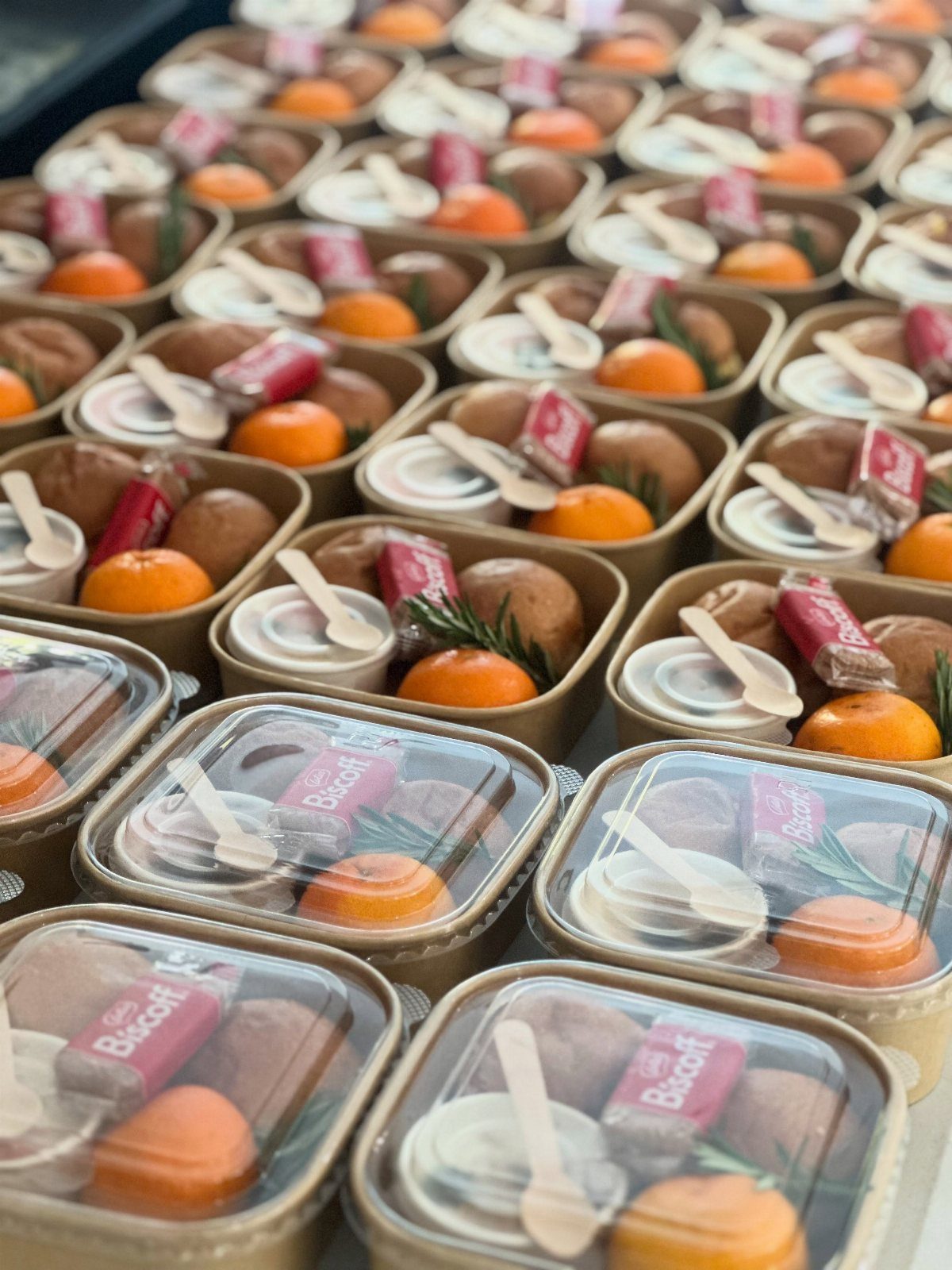 Small cardboard snack boxes containing oranges, pastries, Biscoff cookies, and dip cups.
