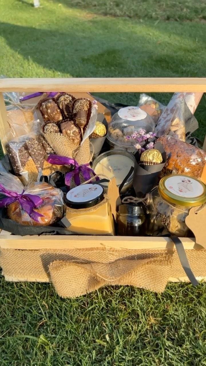 Wooden snack crate filled with jars, cookies, and chocolates on green grass.