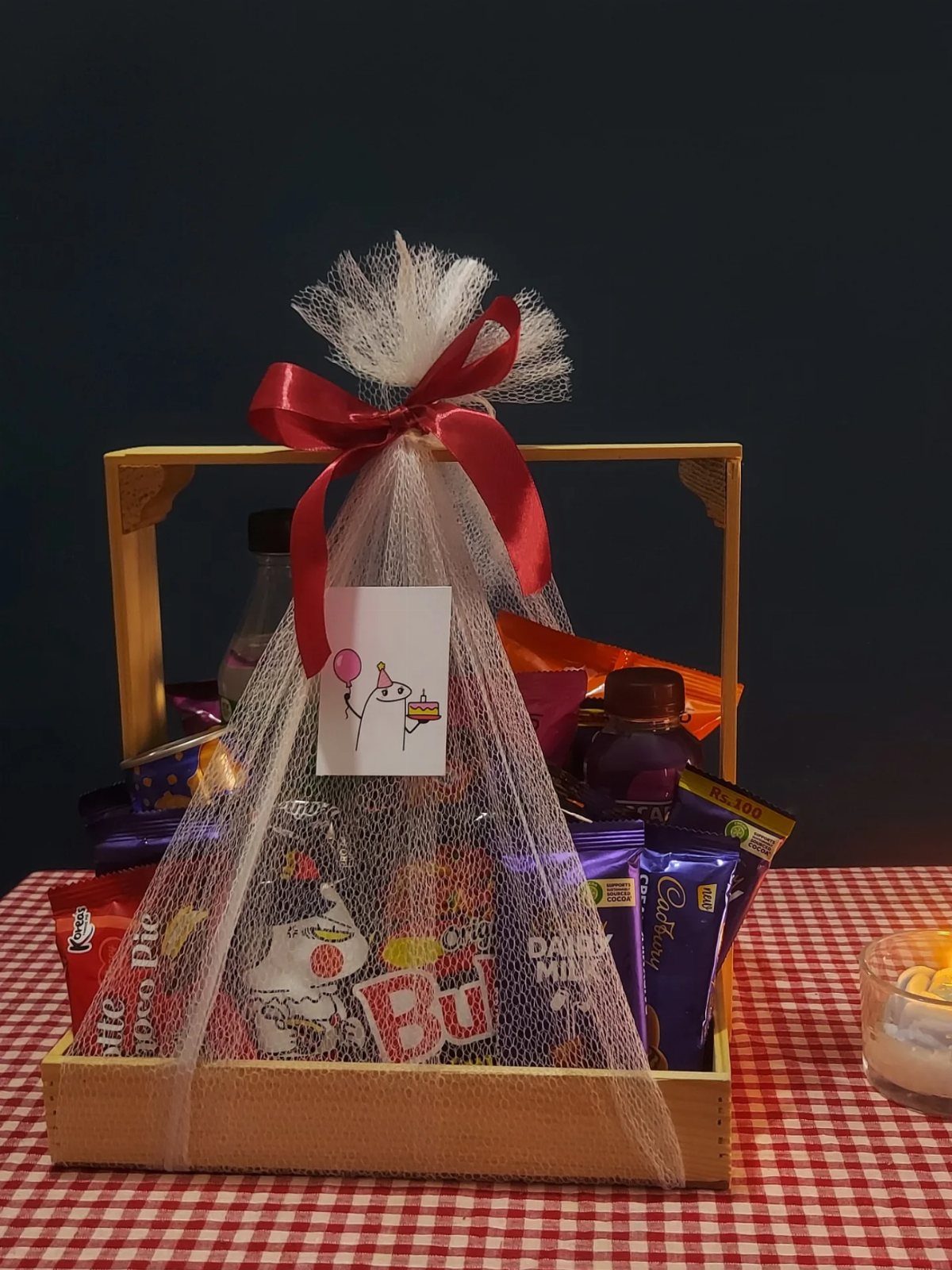 Wooden snack basket filled with chocolates and treats wrapped in white tulle and red ribbon