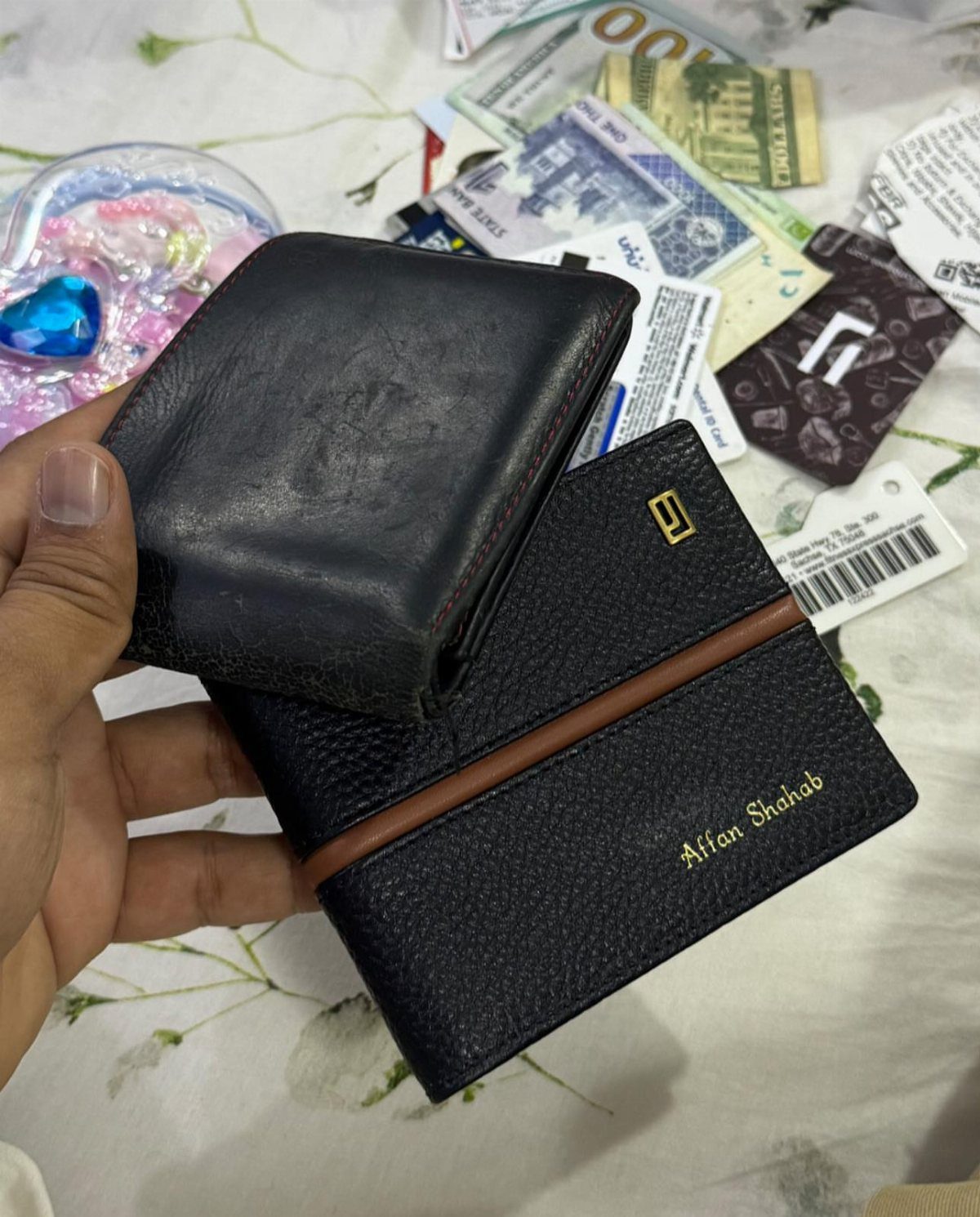 Two black leather wallets, one with gold personalized name embossing and brown detail.