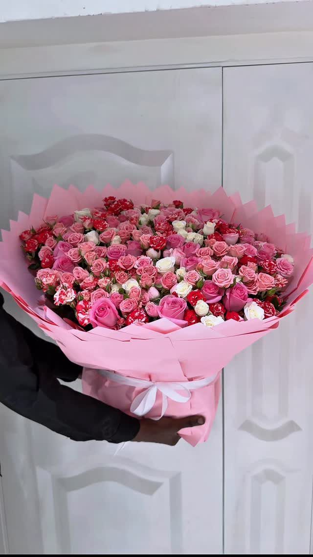 Large bouquet of pink, red, and white roses wrapped in pink paper.