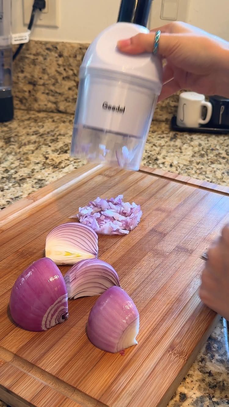 Electric mini food chopper chopping red onions on a wooden cutting board