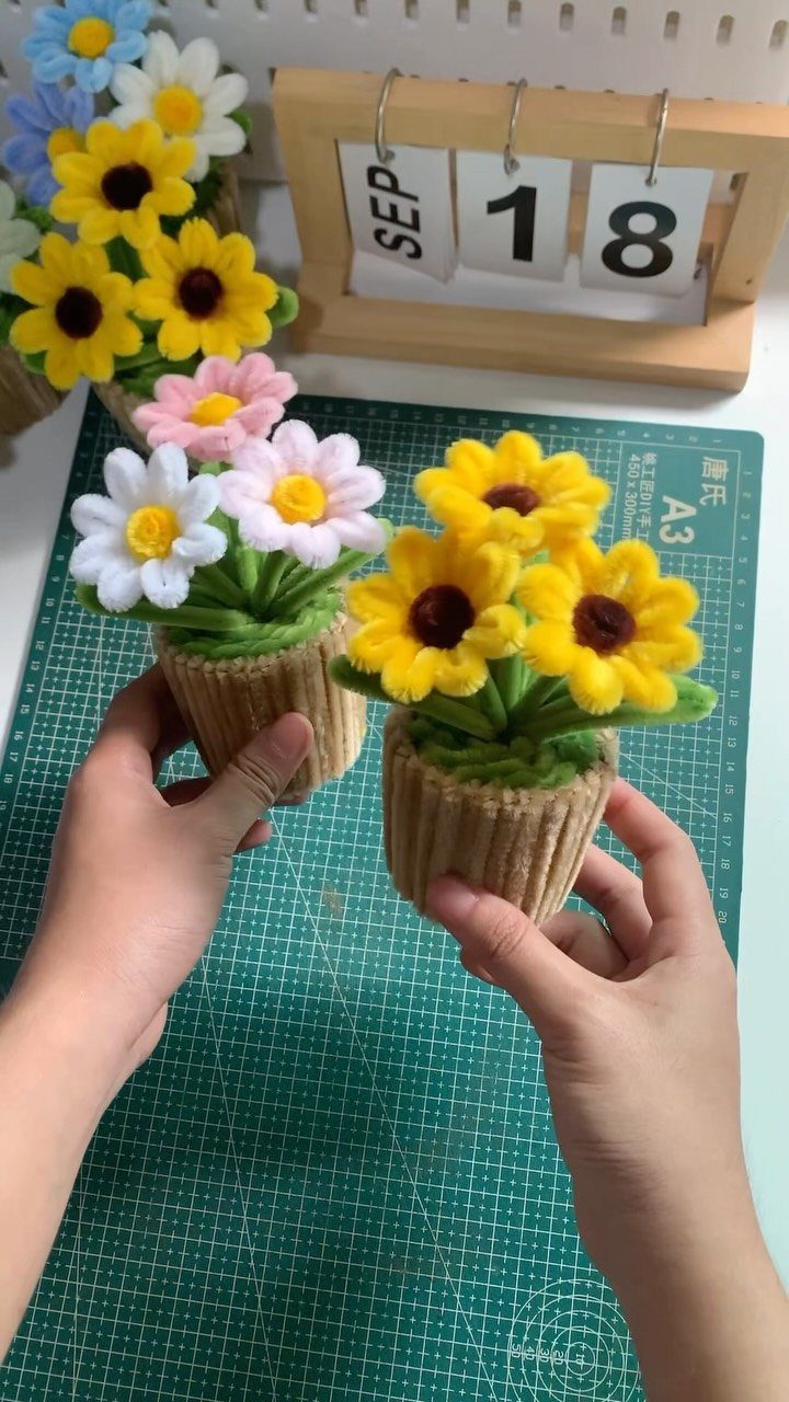 Hands holding small handmade felt flower bouquets in brown ribbed pots.