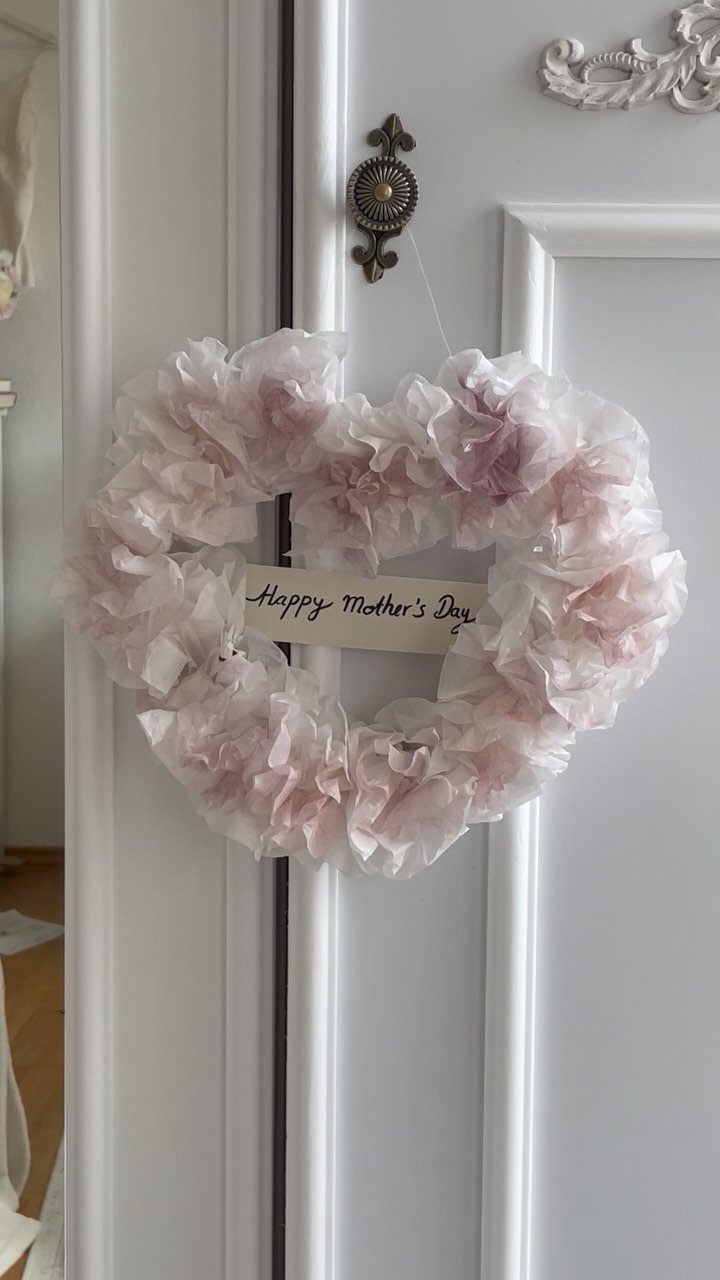 Heart-shaped pink fabric wreath with Happy Mother's Day card hanging on white door