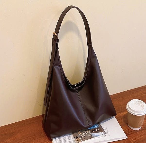 Dark brown leather handbag on a wooden table with a coffee cup and magazine.