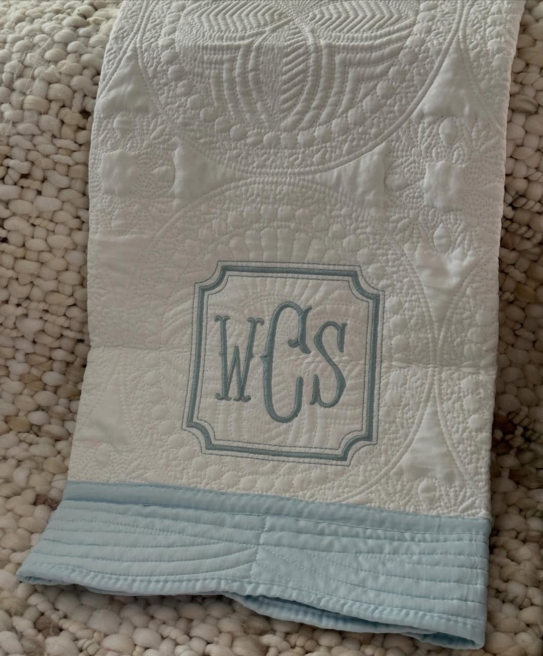 White quilted blanket with light blue border and embroidered monogram WCS.