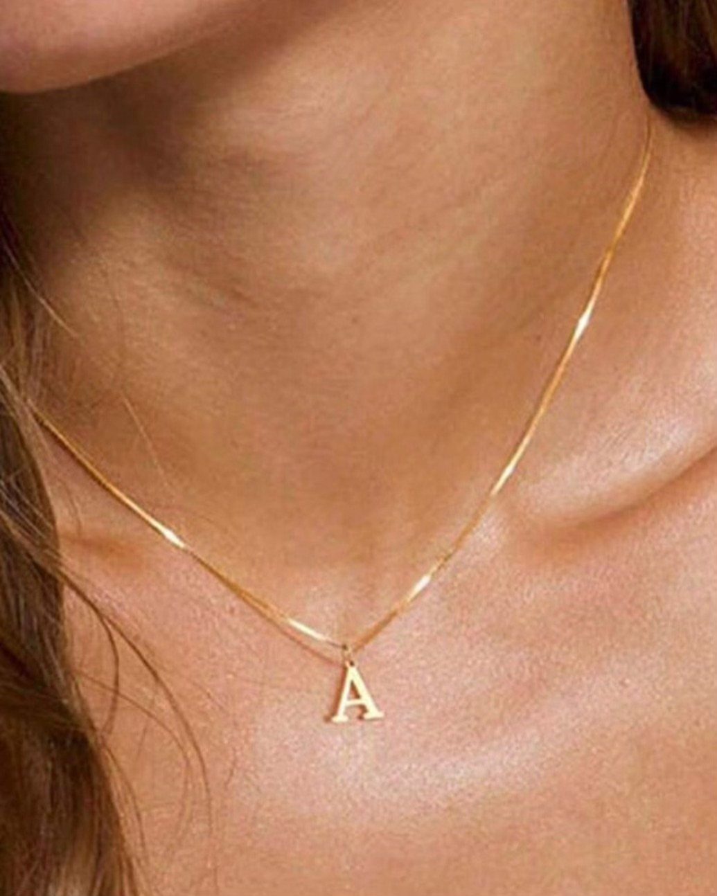 Gold chain necklace with a letter A pendant worn on a person's neck.