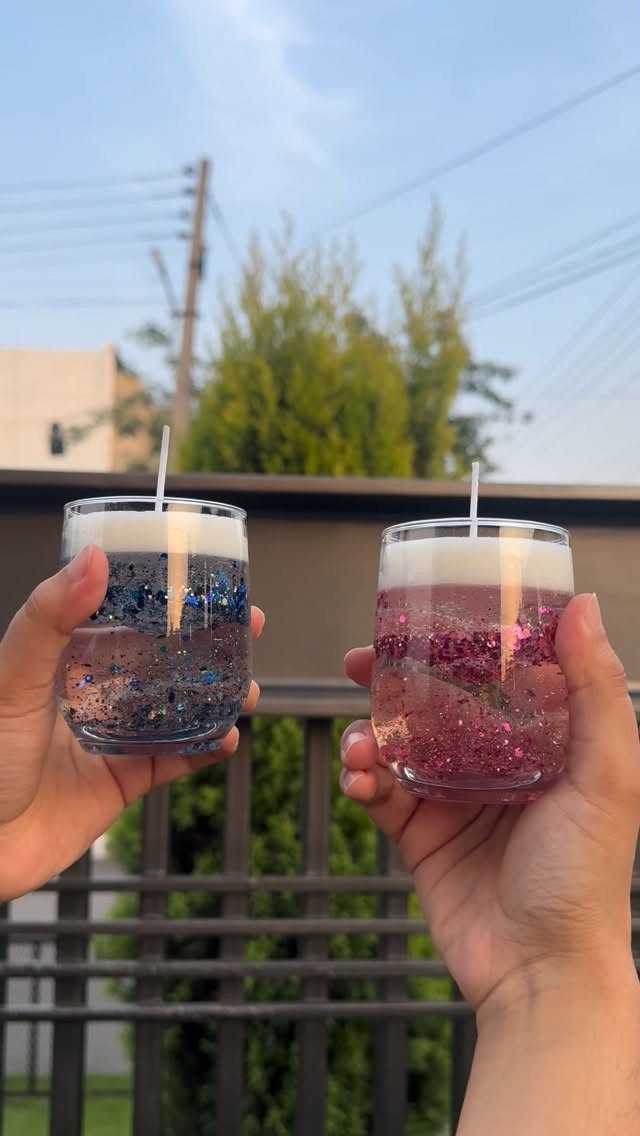 Two glittery glass jar candles held up against a blurred outdoor background.