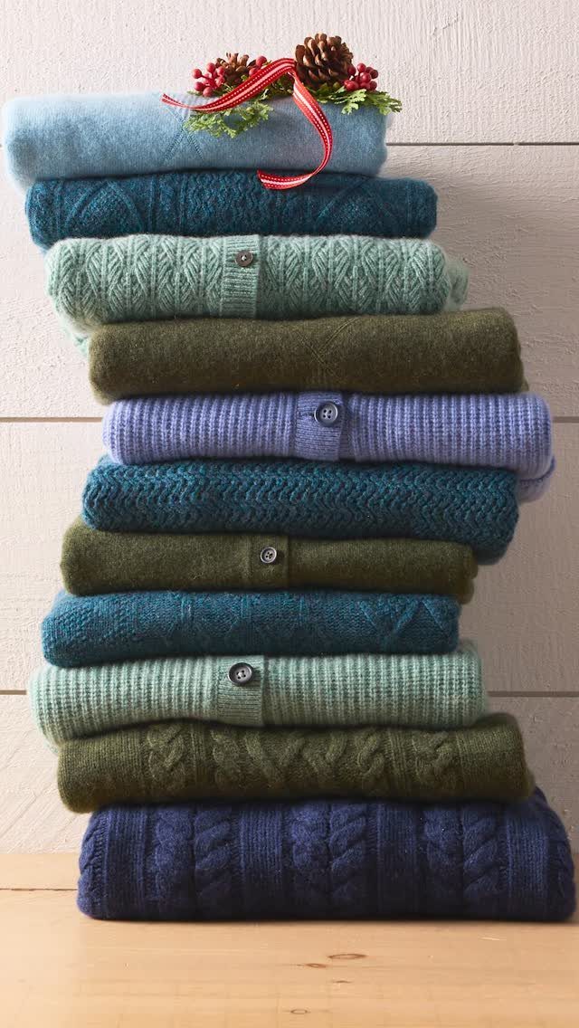 Stacked colorful knit sweaters topped with a red ribbon and pinecone decoration.