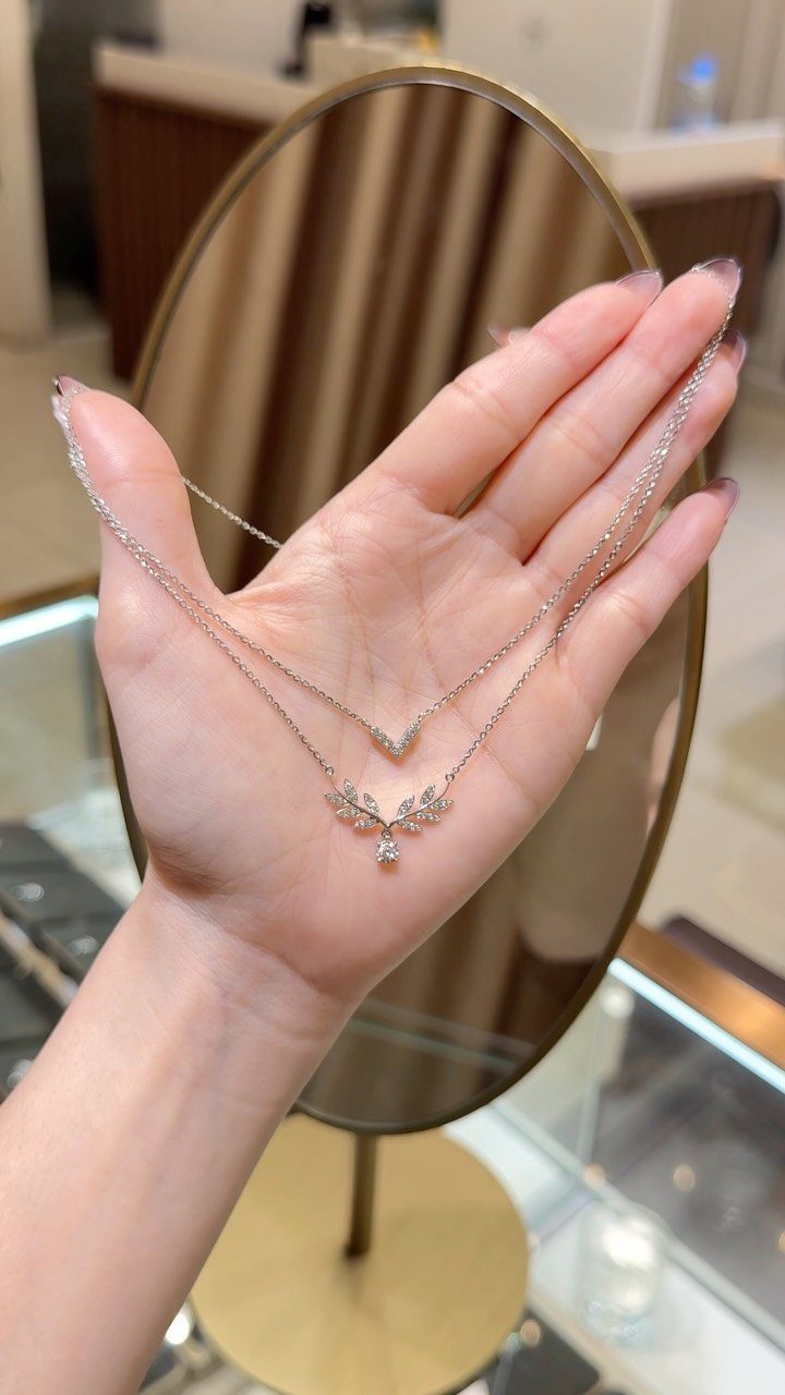 Two silver gemstone necklaces held in an open palm before an oval mirror.