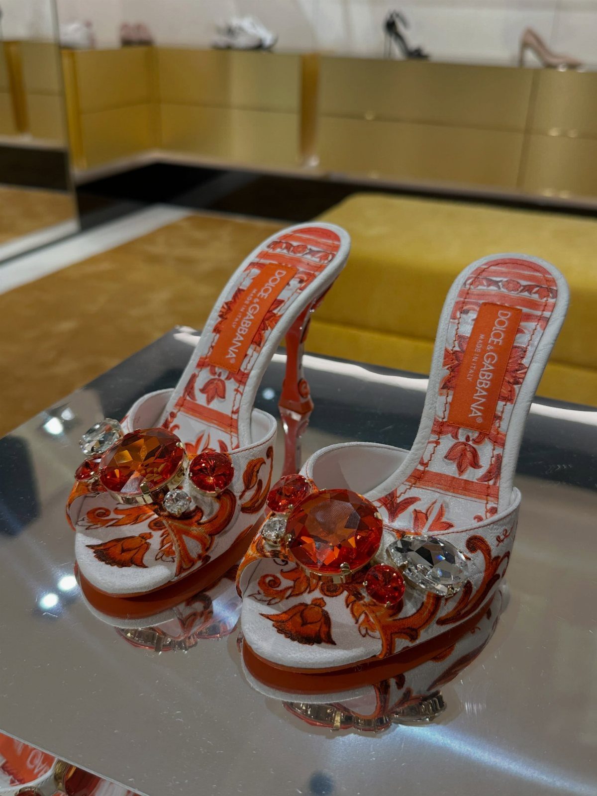 Dolce & Gabbana high-heeled mules with orange patterns and large orange gemstones.