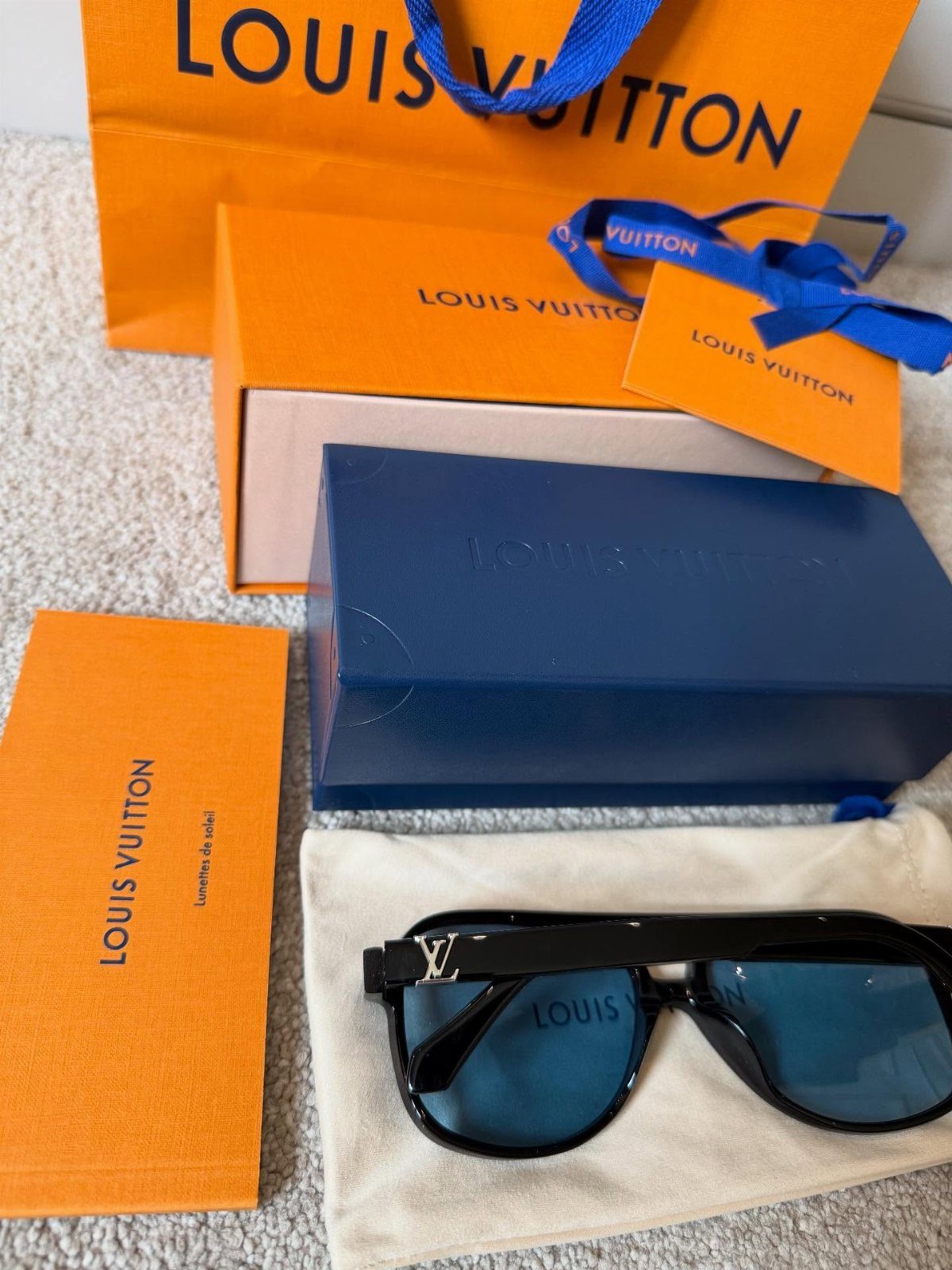 Black designer sunglasses with gold logos and luxury orange and blue packaging.