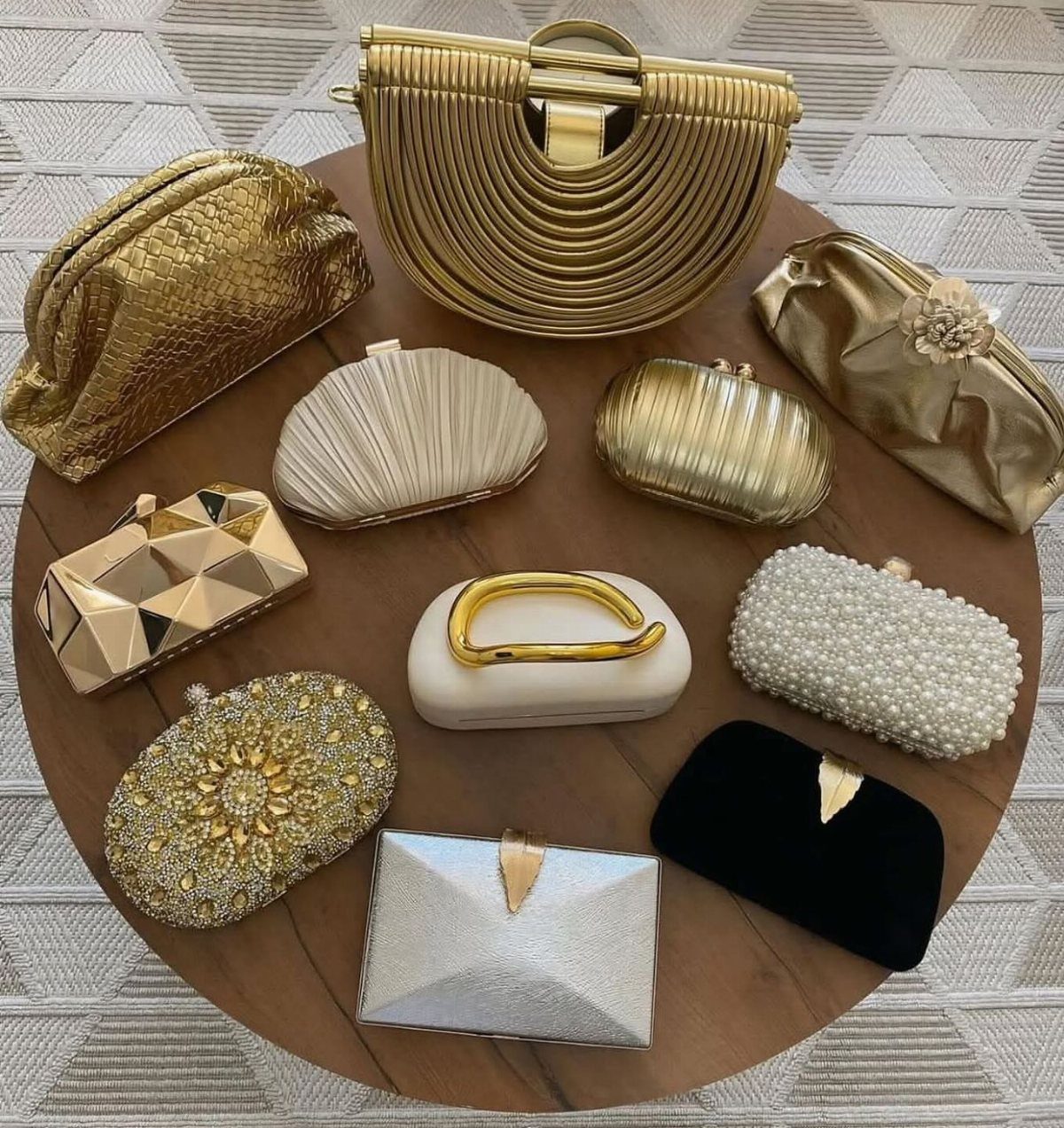 Various luxury evening clutch bags in gold, silver, and black on a wooden table.
