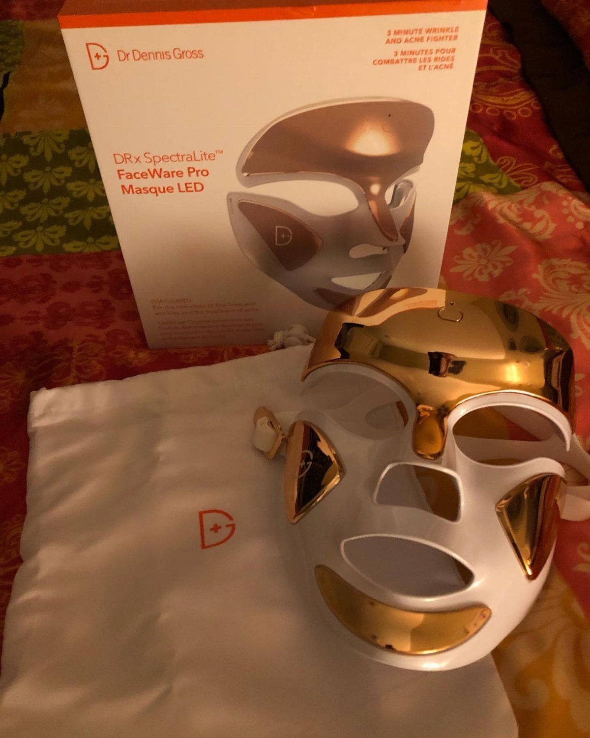 LED face mask with gold accents next to its product packaging and pouch