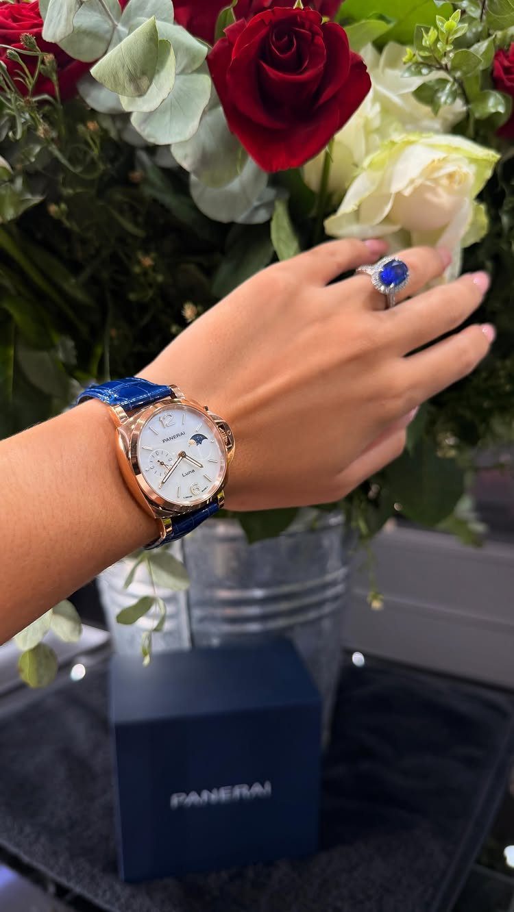 Gold luxury watch with blue strap on a wrist near red roses