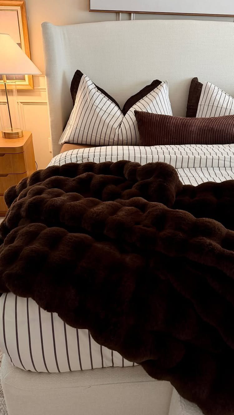 Dark brown plush faux-fur blanket draped over a striped bed with white linens.