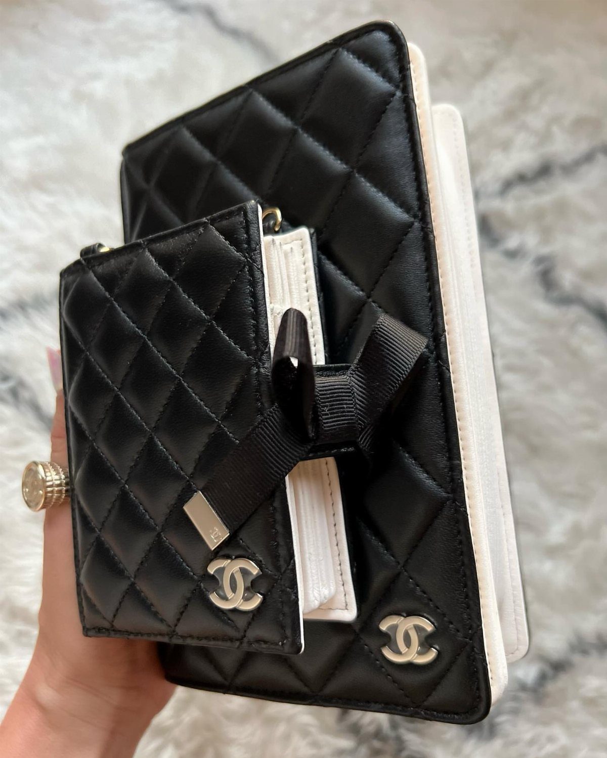 Black quilted leather Chanel wallet and notebook with silver logos held by hand.