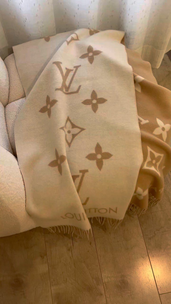 Beige Louis Vuitton monogrammed shawl draped over a white tufted chair.