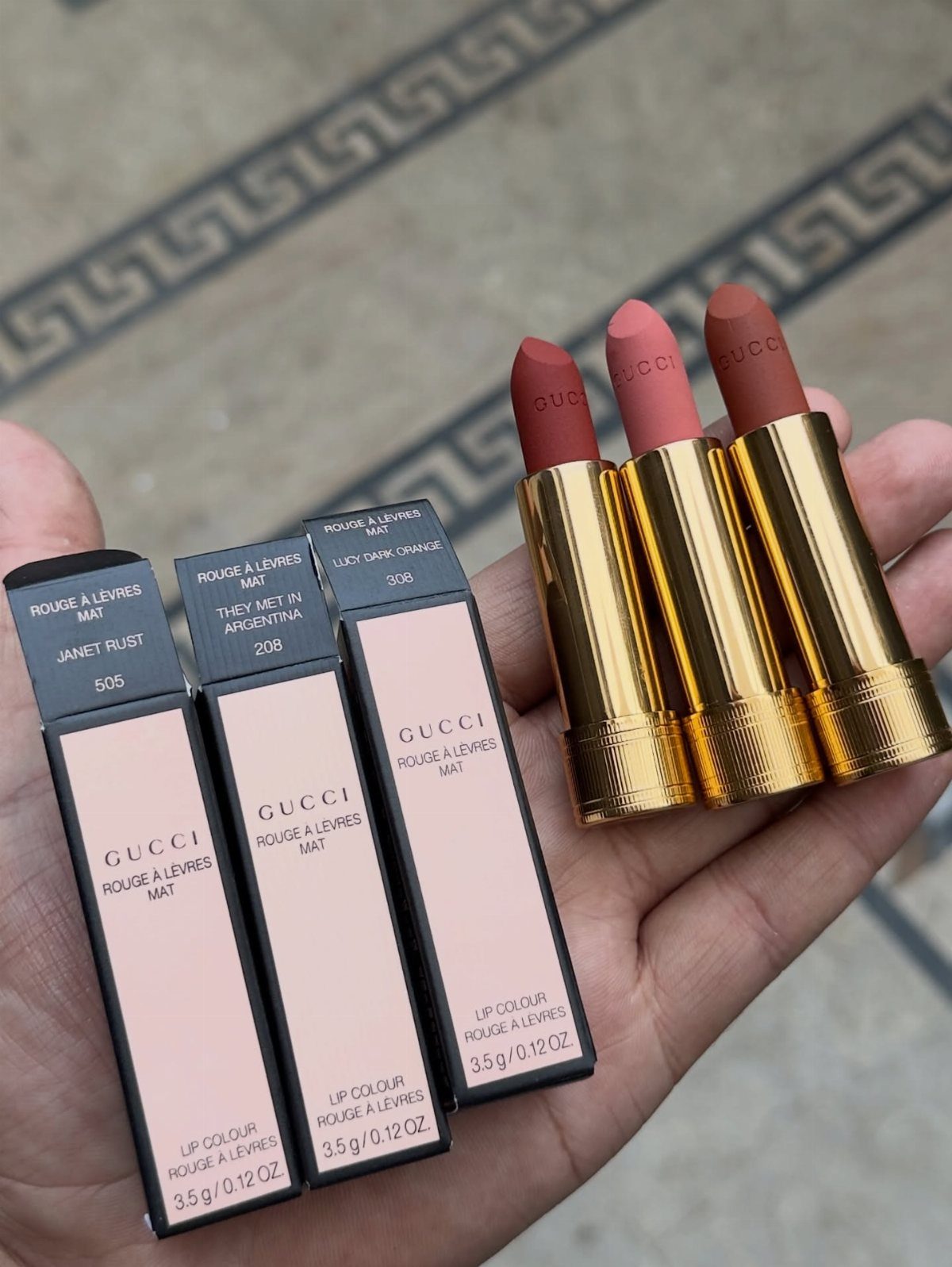 Three gold Gucci lipsticks and their pink boxes held in a person's hand.