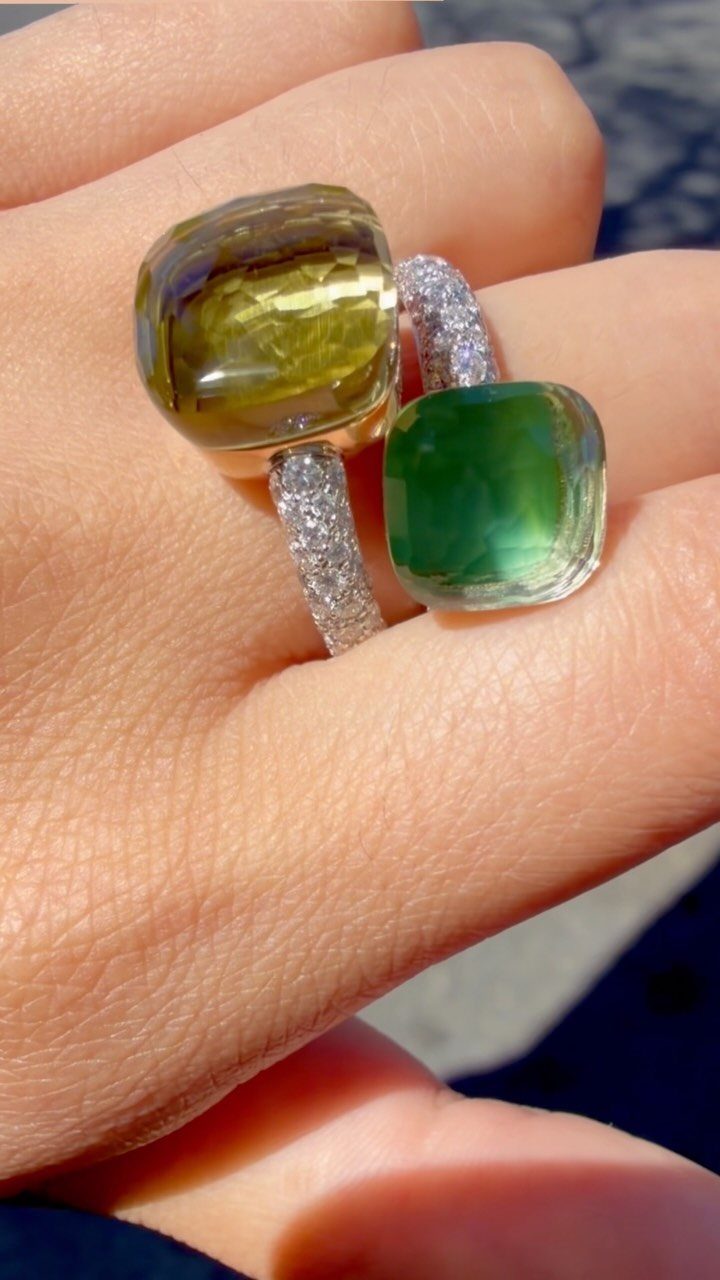 Two chunky rings with yellow and green translucent stones on a hand.