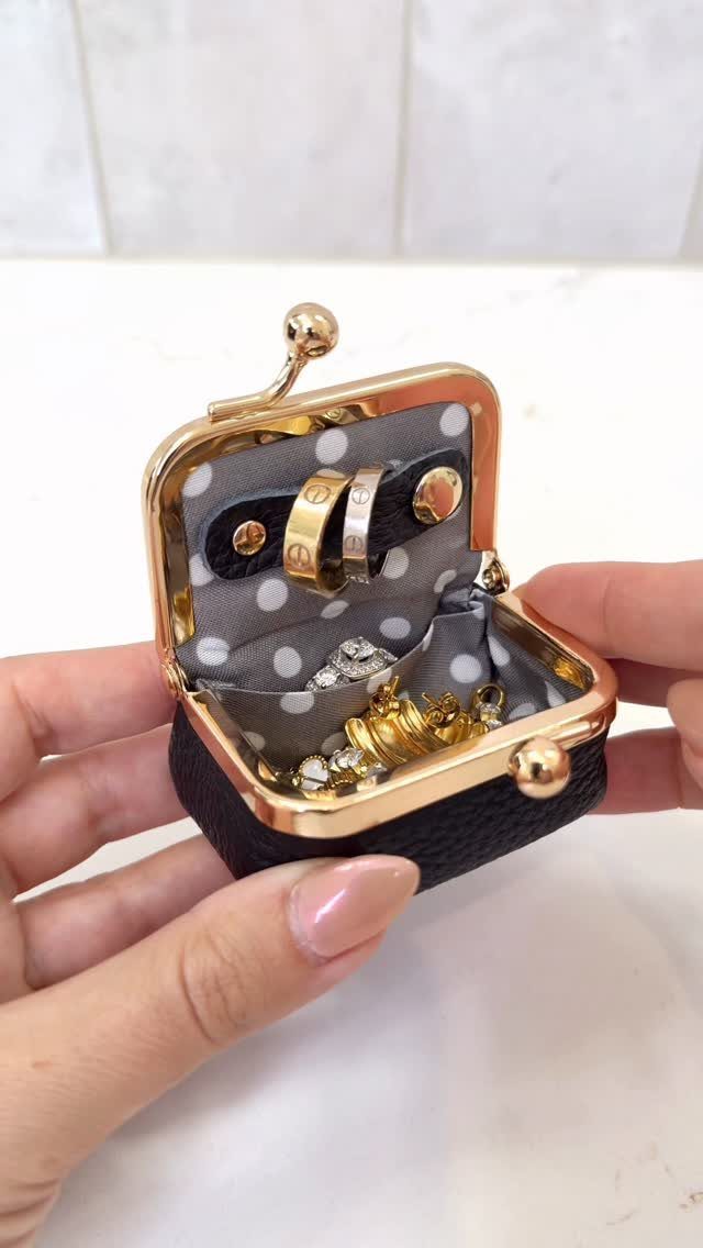 Small black leather jewelry case holding gold rings and sparkling accessories.
