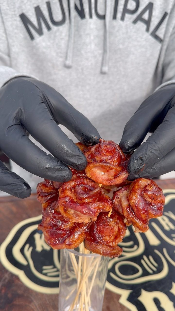 Bacon roses bouquet held by gloved hands in a clear glass vase.
