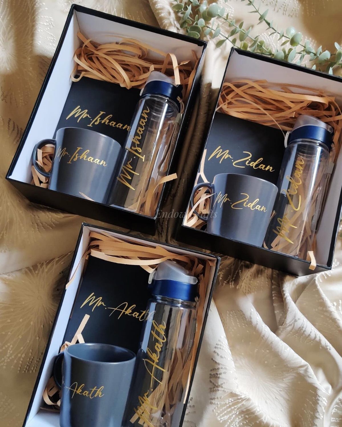 Three personalized gift sets with grey mugs and water bottles in black boxes.